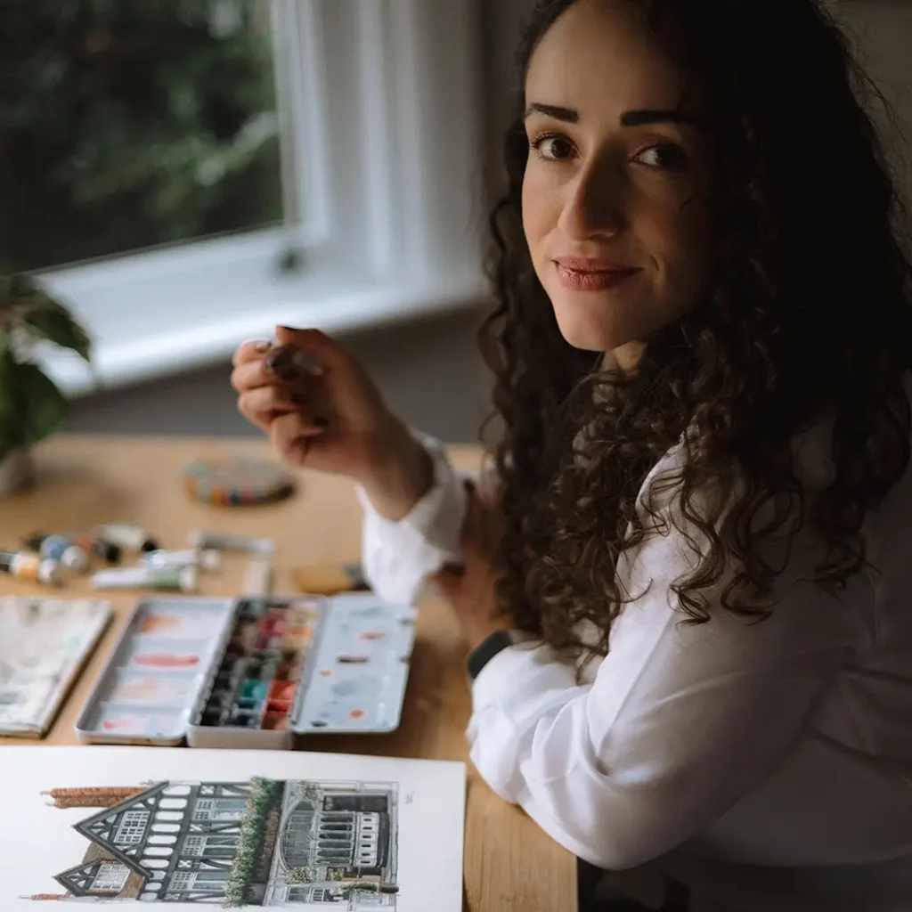 Marina Assis holding a brush while sitting at a table with watercolour materials